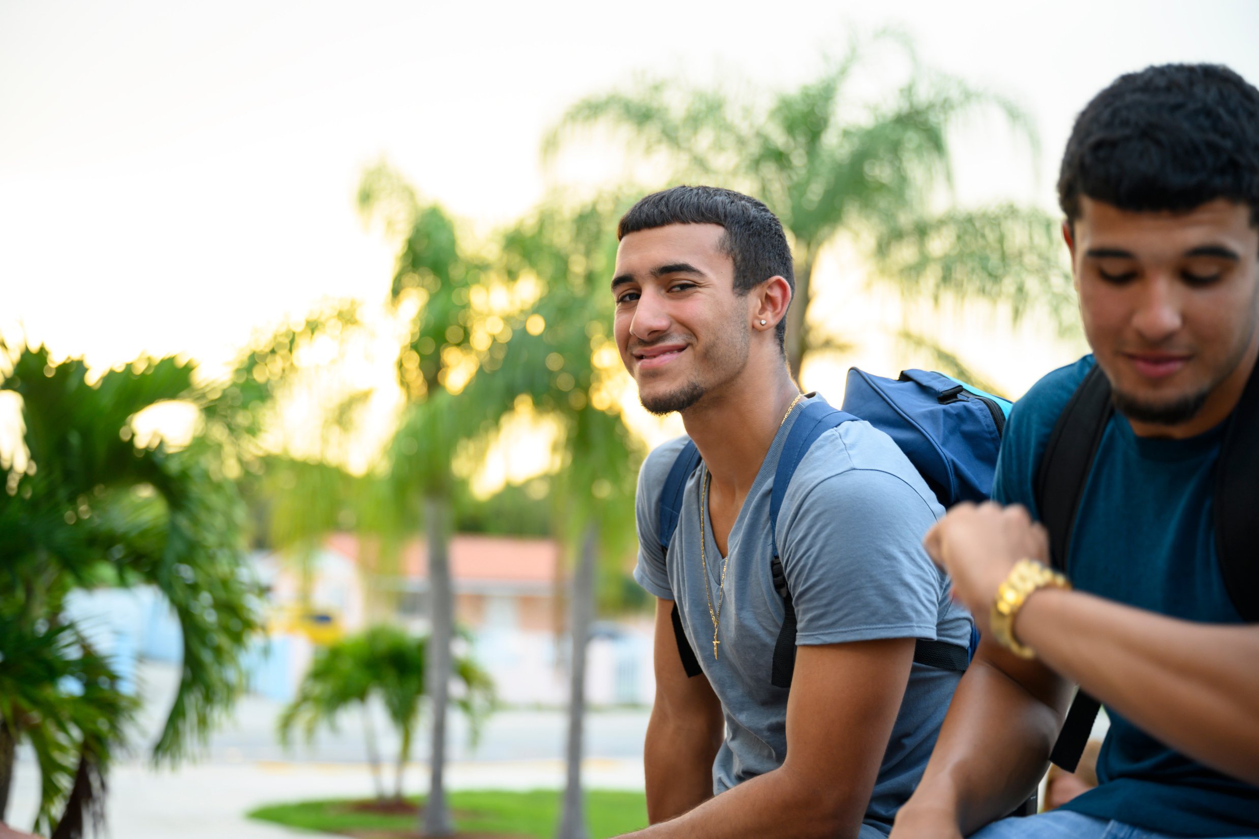 Confident Hispanic high-schooler sitting outside with friend